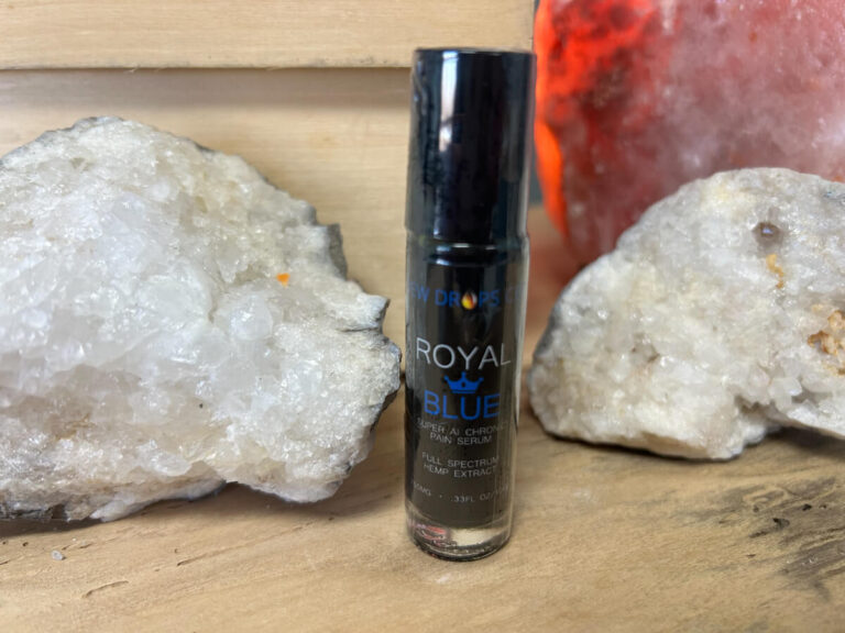 A bottle of royal blue tinted lip balm sitting next to some rocks.